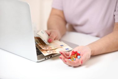 Bilgisayarında para, euro nakit para ve haplar olan yaşlı bir kadın, kopyalama alanı. Tedavi maliyeti, ilaç fiyatı, sağlık sigortası bütçesi.