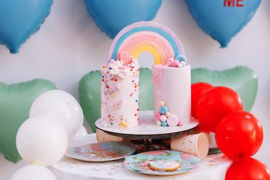 Gökkuşaklı büyük doğum günü pastası, renkli serpintiler. Bir çok renkli kalp balonunun arka planında. Doğum günü partisi. Güzel tatil.