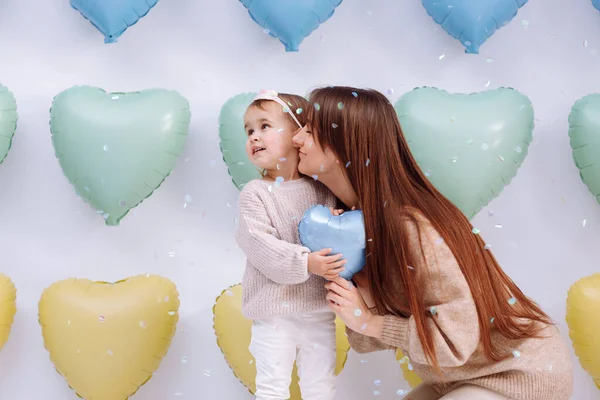 美しい若い母親と小さなかわいい娘が一緒にカラフルなハートバルーンの背景に立って 青いバレンタインバルーンを保持しています 誕生日 ベレンタイン 母の日 — ストック写真