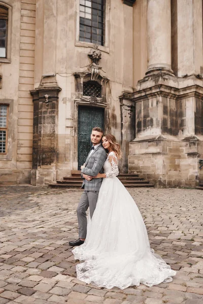 スタイリッシュな花嫁と新郎が優しくヨーロッパの街の通りに抱きつく 近くの古代の建物を受け入れる新婚夫婦の豪華な結婚式 ロマンチックな瞬間だ 結婚式の — ストック写真