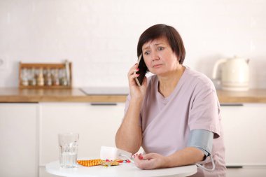 Çevrimiçi doktor konsültasyonu, uzaktan tıbbi yardım, yaşlılar ve sağlık hizmetleri. Hasta, yaşlı bir kadın. Cep telefonuyla doktorla konuşuyor. Kan basıncını ölçüyor..