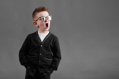 Gri arka planda ağzı açık bir çocuk. Komik gözlüklü çocuk. Komik asık suratlı küçük çocuk..