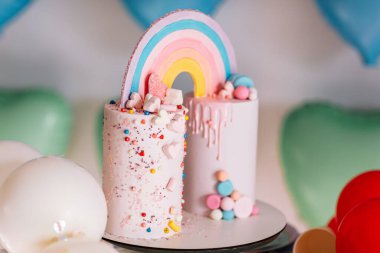 Gökkuşaklı büyük doğum günü pastası, renkli serpintiler. Bir çok renkli kalp balonunun arka planında. Doğum günü partisi. Güzel tatil.