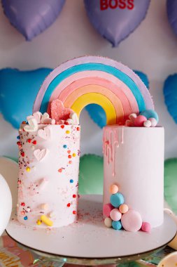 Gökkuşaklı büyük doğum günü pastası, renkli serpintiler. Bir çok renkli kalp balonunun arka planında. Doğum günü partisi. Güzel tatil.