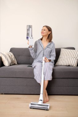 Kanepede ve evinde oturan şarj edilebilir elektrikli süpürgeyle genç bir kadın. Kız elektrik süpürgesini talimatlara göre katlamaya çalışıyor..