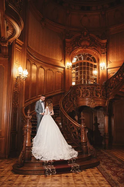 婚礼当天 身穿白色长裙的漂亮新娘和身穿黑色西服的年轻新郎拥抱着欧洲历史建筑 — 图库照片