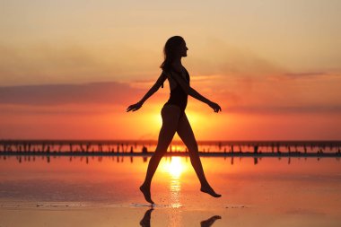 Gün batımında denizde dans eden mayolu zayıf bir kadının silueti. yaz tatili.