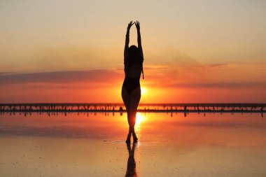 Gün batımında denizde dans eden mayolu zayıf bir kadının silueti. yaz tatili.