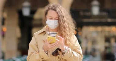 Gün boyunca şehir sokaklarında uzun kıvırcık saçlı, güneş gözlüğü takan ve hava kirliliğine ve Coronavirus Covid 19 'a karşı maske takan güzel bir kadın.. 