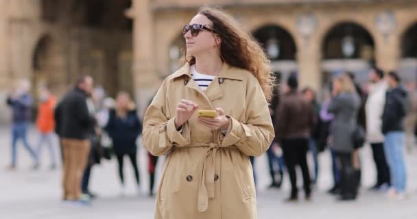 Piękna młoda kobieta z długimi kręconymi włosami nosi okulary przeciwsłoneczne i używa telefonu komórkowego. dziewczyna na zewnątrz i na ulicach miasta w ciągu dnia — Wideo stockowe