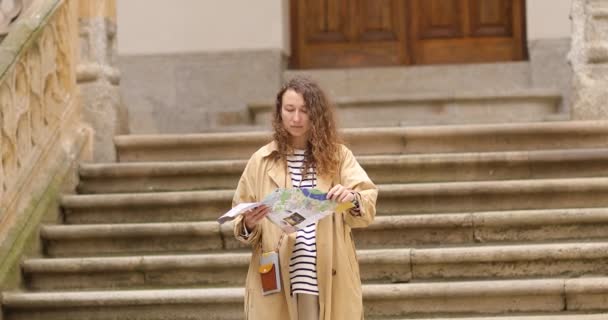 Jeune belle voyageuse descend la rue tenant une carte en papier. Fille élégante touristique avec carte en papier fait du tourisme en plein air — Video