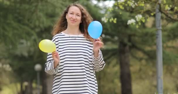 Glimlachende vrouw met blauwe en gele luchtballonnen in de buitenlucht. Oekraïense meisje in gestreepte blouse met ballonnen kleuren van de vlag van Oekraïne — Stockvideo