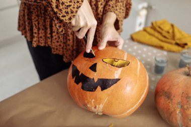 Genç kadının Jack O Lattern onun ahşap mutfak masasında bıçakla olgun Turuncu kabak oyma kapatın. Tüm hazırlama kadın Havva Halloween parti süslemeleri toplantı salonu. Arka plan, kopya alanı