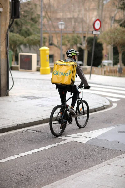España, Salamanca - 3 de abril de 2022: Entrega de alimentos y comestibles. El mensajero de bicicletas, con una mochila termo amarilla, la empresa Glovo, entrega los bienes necesarios a los residentes de la ciudad — Foto de Stock