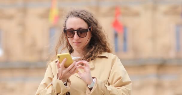 Femme parler au téléphone portable à l'extérieur de la rue de la ville. Touriste joyeux dans les lunettes de soleil s'amuser à marcher dans les rues de la vieille ville d'Espagne, parler sur un téléphone portable tout en itinérance. — Video