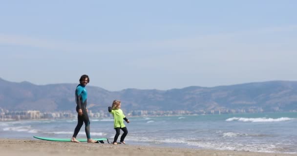 Castellon, Spanien-april 2022: far lär sitt barn surfa på stranden vid havet. upphetsad flicka eller pojke gör exekverar utveckla nya färdigheter. Surfing, faderskap — Stockvideo