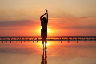 Gün batımında denizde dans eden mayolu zayıf bir kadının silueti. yaz tatili.