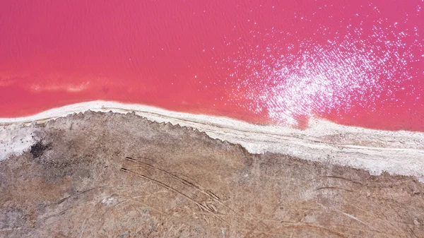 Pembe bir tuz gölünün üzerinde uçuyor. Tuz üretim tesisleri tuzlu göldeki tuz buharlaştırma göleti tarlaları. Dunaliella tuzlu kuru kristalize edilmiş tuzlu kıyılarla mineral gölüne kırmızı, pembe bir su döker.
