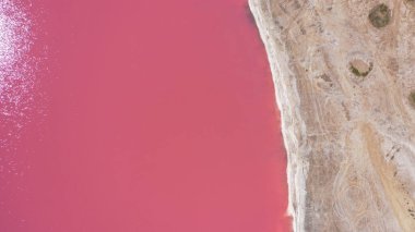 Pembe bir tuz gölünün üzerinde uçuyor. Tuz üretim tesisleri tuzlu göldeki tuz buharlaştırma göleti tarlaları. Dunaliella tuzlu kuru kristalize edilmiş tuzlu kıyılarla mineral gölüne kırmızı, pembe bir su döker..