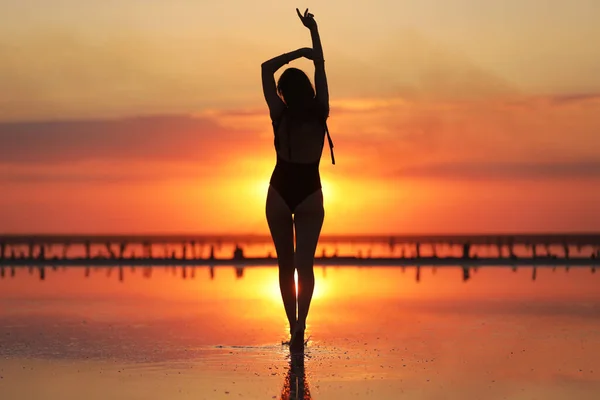 Silhouette di una giovane donna magra in costume da bagno che balla al tramonto sul mare. vacanze estive — Foto Stock