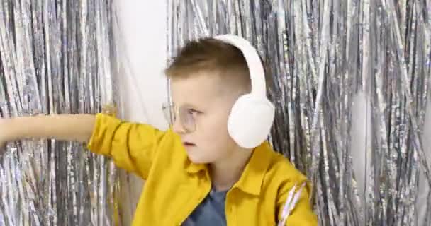 Un niño europeo pequeño con grandes auriculares blancos y baila activamente y escucha música. El concepto de la música, el ocio en casa. Imágenes de alta calidad 4k — Vídeos de Stock