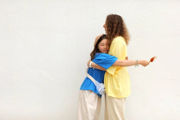 Femme heureuse en t-shirt jaune basique s'amuse avec enfant fille 10-11 ans en t-shirt bleu. Maman d'une petite fille isolée sur fond blanc. Fête des mères amour famille. — Photo