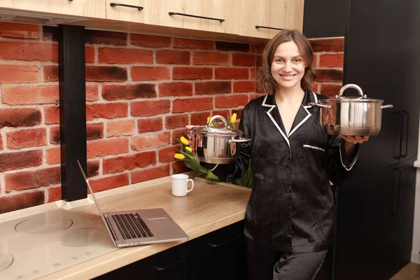 Çevrimiçi aşçılık dersi. Modern mutfakta elinde tencereyle blog yazarken dizüstü bilgisayar kullanan bir kadının kesilmiş fotoğrafı..