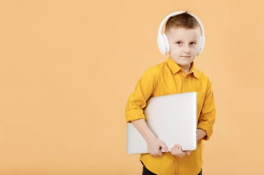 Sarı tişörtlü, kulaklıklı, dizüstü bilgisayarı olan komik, zeki bir öğrencinin portresi. Sarı stüdyo geçmişi. Eğitim. Kameraya bakıyorum. Yüksek kalite fotoğraf.