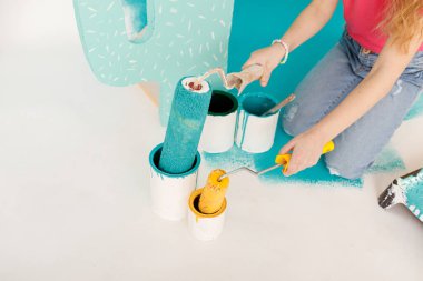 Sevimli küçük kız apartman dairesinde tamirat yapıyor eğlence duvarı boyuyor. Stüdyoda boya rulosu ve büyük kağıt kaktüsüyle gülümseyen güzel bir çocuğun portresi. Neşeli şirin bebek eğleniyor.