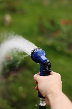 Bahçıvanın eli bir hortumu spreyle tutuyor ve bahçedeki bitkileri suluyor.