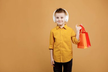 Elinde hediyeler ya da sarı arka planda alışveriş torbaları olan gülümseyen bir çocuk resmi. Beyaz kulaklıklı çocuk. Bir sürü renkli kağıt torbası olan bir müşteri. Tatil satışları ve indirimler. Siber Pazartesi.