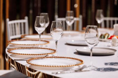 Restoranda boş cam seti. düğün, dekor, kutlama, tatil konsepti - beyaz masa örtülü romantik masa örtüsü, tabak, kristal gözlük.