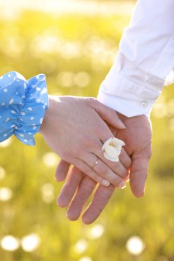 Romantik randevu konsepti. Genç adam ve kadın el ele tutuşuyorlar. Elinde papatya çiçeğiyle mavi elbiseli altın yüzüklü kız..