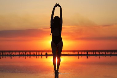 Gün batımında denizde dans eden mayolu zayıf bir kadının silueti. yaz tatili.