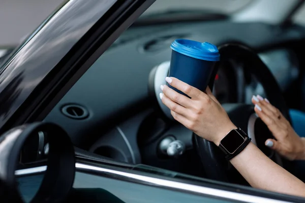 cropped photo of woman\'s hand holding blue paper cup of coffee in car. Hot drink take away. Travel with coffee. Concept of coffee with you. Mockup.