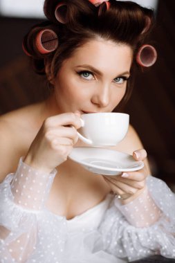 Gülümseyen kadının güzel portresi. Makyajlı, beyaz elbiseli, evde dinlenen kahve ya da çay içen ve kameraya bakan güzel bir kadın..