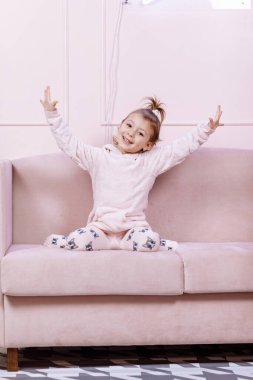 Küçük sevimli beyaz kız pembe kanepede tek başına uzanıyor ve odadaki kameraya bakıyor. Yüksek kalite fotoğraf.