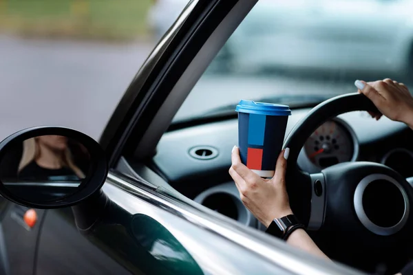 cropped photo of woman\'s hand holding blue paper cup of coffee in car. Hot drink take away. Travel with coffee. Concept of coffee with you. Mockup.