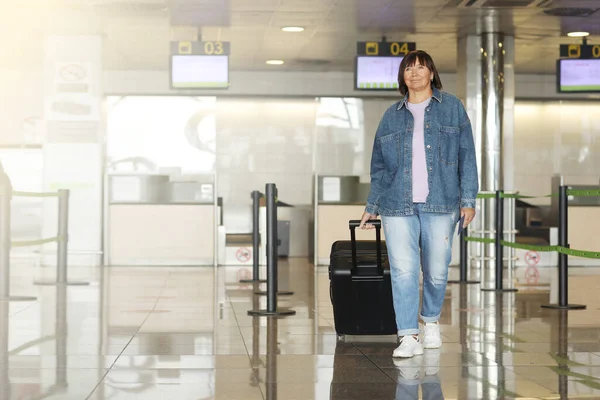 middle aged woman traveling in casual clothes. Female in airport with suitcase and passport going after check-in desk in for her flight. Passenger travel abroad on holiday or weekend