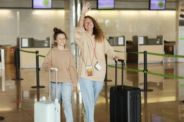 10代の娘とスーツケースを持った笑顔の若い母親が空港に到着した飛行機の後に会う人に手を振っています 休暇旅行 家族との時間 — ストック写真