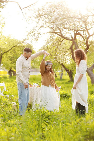 Счастливая семья в отпуске. Мама, папа и маленькая девочка расслабляются и наслаждаются ужином вместе в зеленом парке на летнем закате. День матери, отца и ребенка