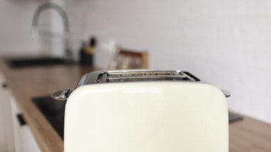 Mutfaktaki tost makinesine tost ekmeği koyuyorlar. Kahvaltı için kızarmış ekmek ve kızarmış ekmek yapmak için mutfak aletleri de dahil. Bir adamın eli ekmek kızartma makinesine bir dilim ekmek sokuyor..