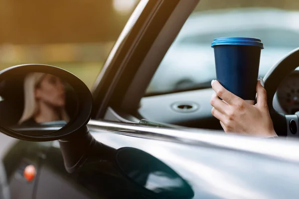 cropped photo of woman\'s hand holding blue paper cup of coffee in car. Hot drink take away. Travel with coffee. Concept of coffee with you. Mockup.