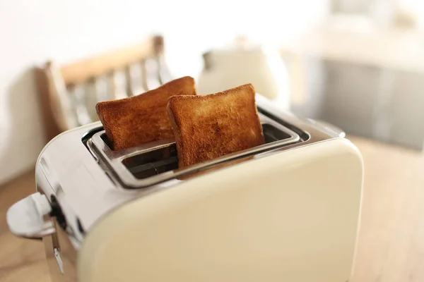 Toasted bread and toaster for breakfast. Modern white toaster and roasted bread slices toasts inside on wooden table in kitchen