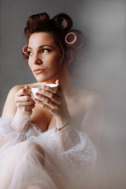 Güzellik portresi kadın. Makyajlı, beyaz elbiseli, evde dinlenen kahve ya da çay içen ve kameraya bakan güzel bir kadın. Uluslararası Kadınlar Günü.