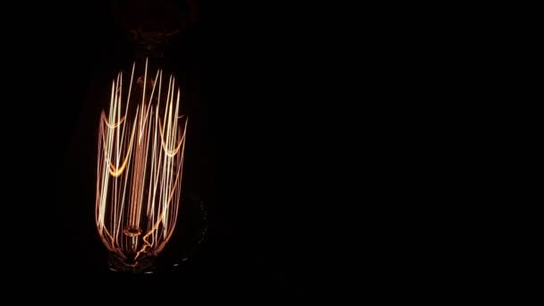 在黑色背景上关闭复古灯泡 钨丝上闪烁着温暖的橙色光芒 螺旋状的震动与电 — 图库视频影像