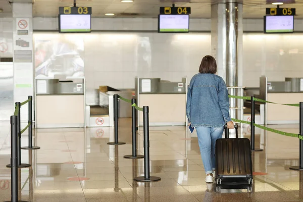 back view of middle aged woman traveling in casual clothes. Female in airport with suitcase going at the check-in desk while checking in for her flight. Passenger travel abroad on holiday or weekend.