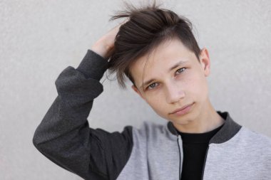 Şık saç kesimi olan yakışıklı bir genç. Gençlik saç stili bir gencin portresi gri arka planda duruyor ve kameraya bakıyor.