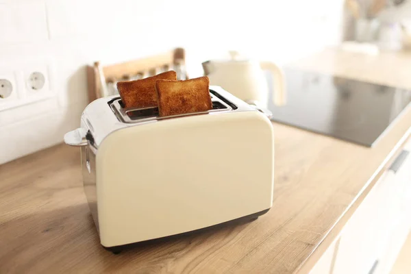 Toasted bread and toaster for breakfast. Modern white toaster and roasted bread slices toasts inside on wooden table in kitchen
