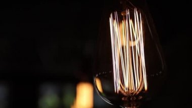 Siyah arkaplandaki retro ampulü kapat. Tungsten iplikleri sıcak turuncu bir ışıkla parıldıyor. Sarmal elektrikle titreşir.